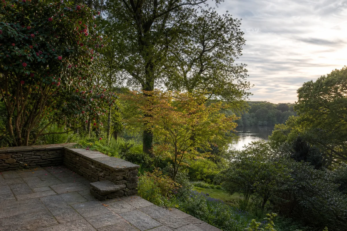 Terrasse en pierre de granit surplombant un jardin arboré près d’une rivière
